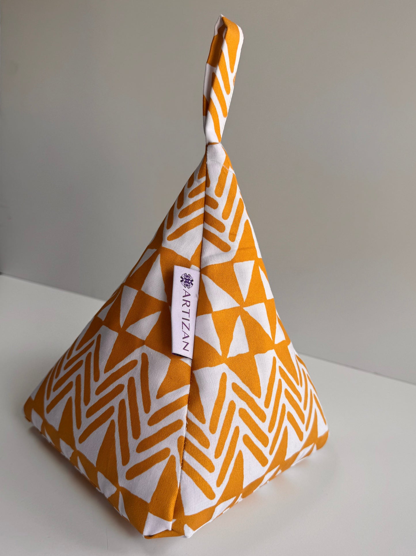 Pyramid-shaped doorstop made using white fabric with gold triangle patterns printed on.