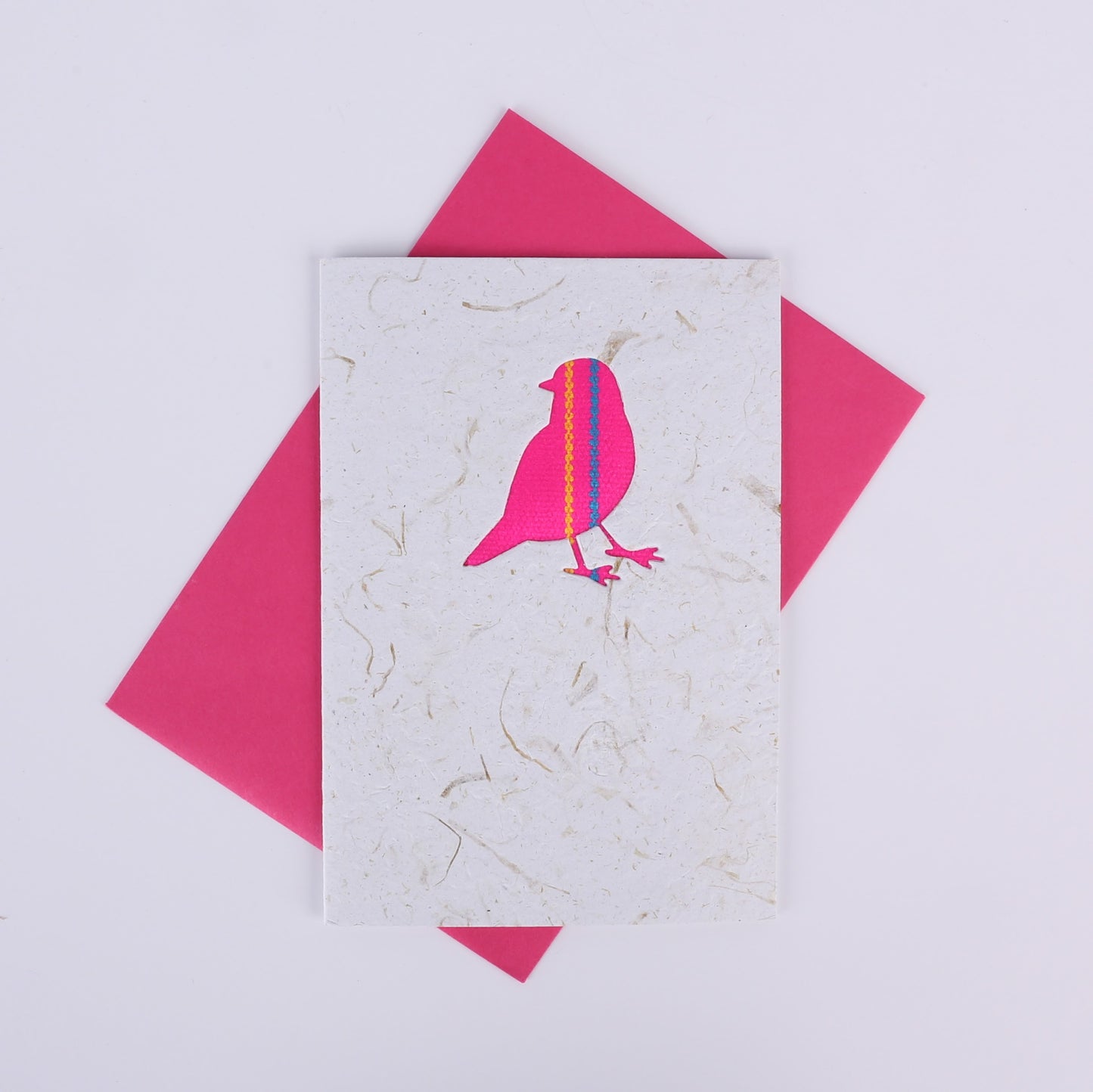 Colourful patterned bird cutout on a white card with a pink envelope underneath