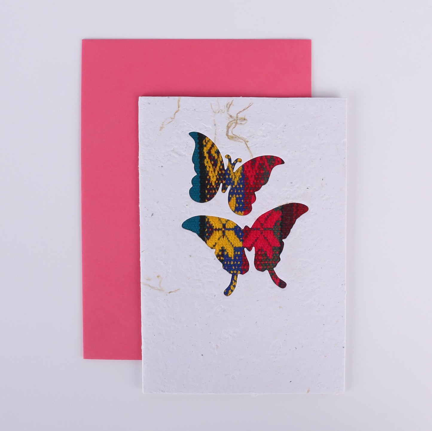 Colourful patterned butterfly cutouts on a white card with a pink envelope underneath