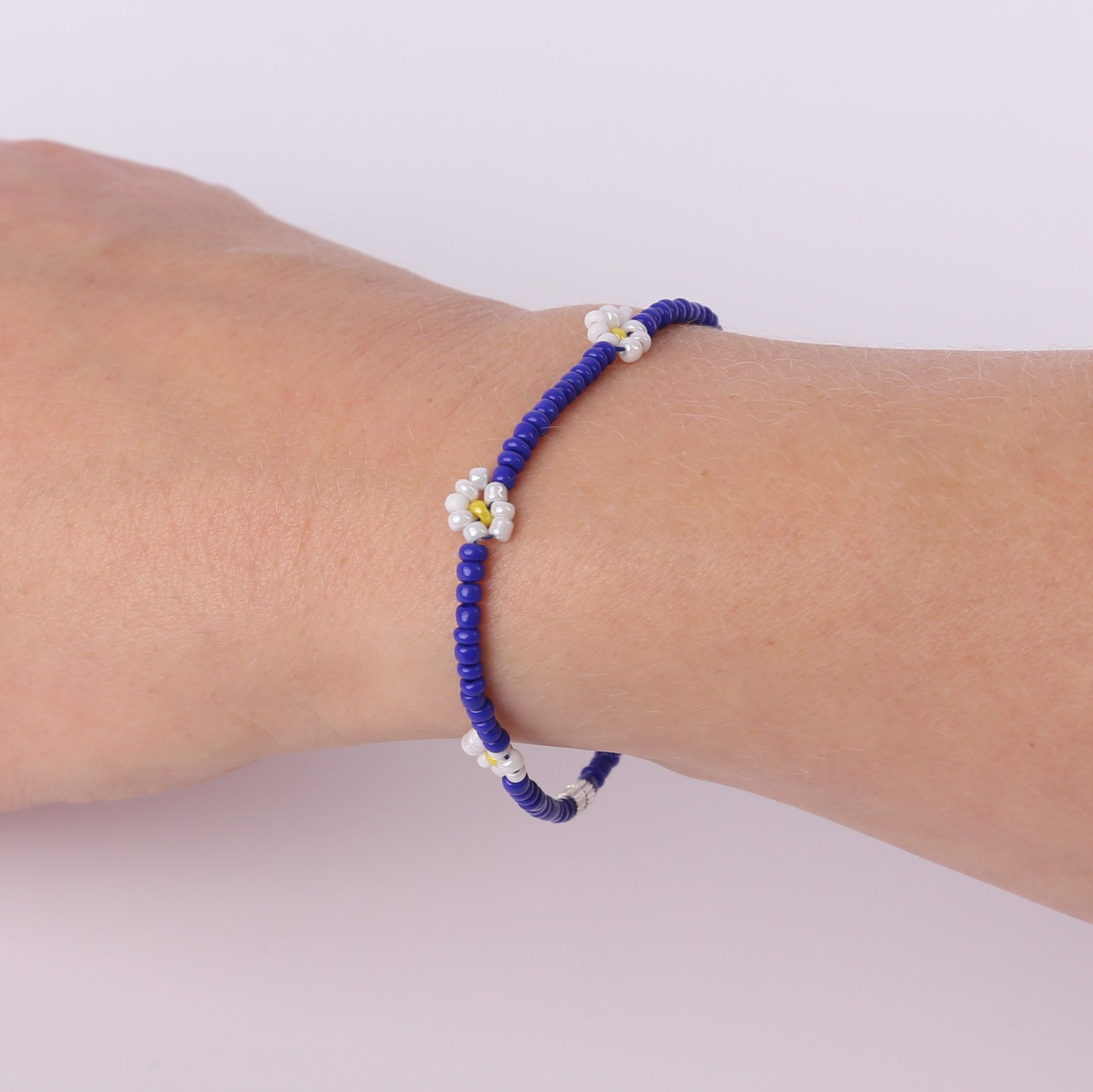Blue beaded bracelet with white daisies on a wrist