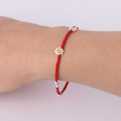 Red beaded bracelet with white daisies on a wrist