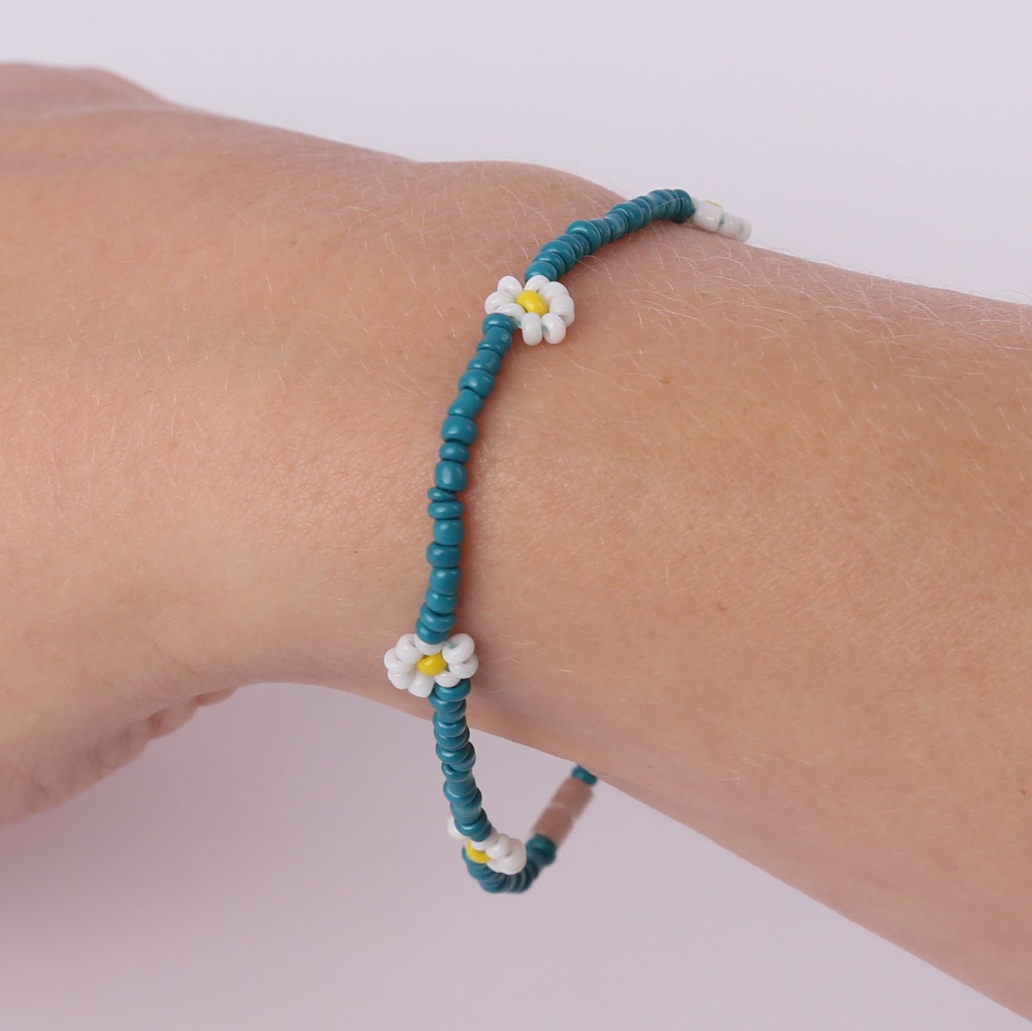 Teal beaded bracelet with white daisies on a wrist