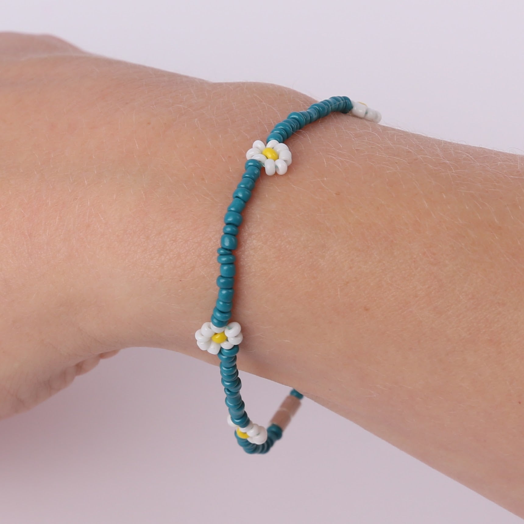 Teal beaded bracelet with white daisies on a wrist