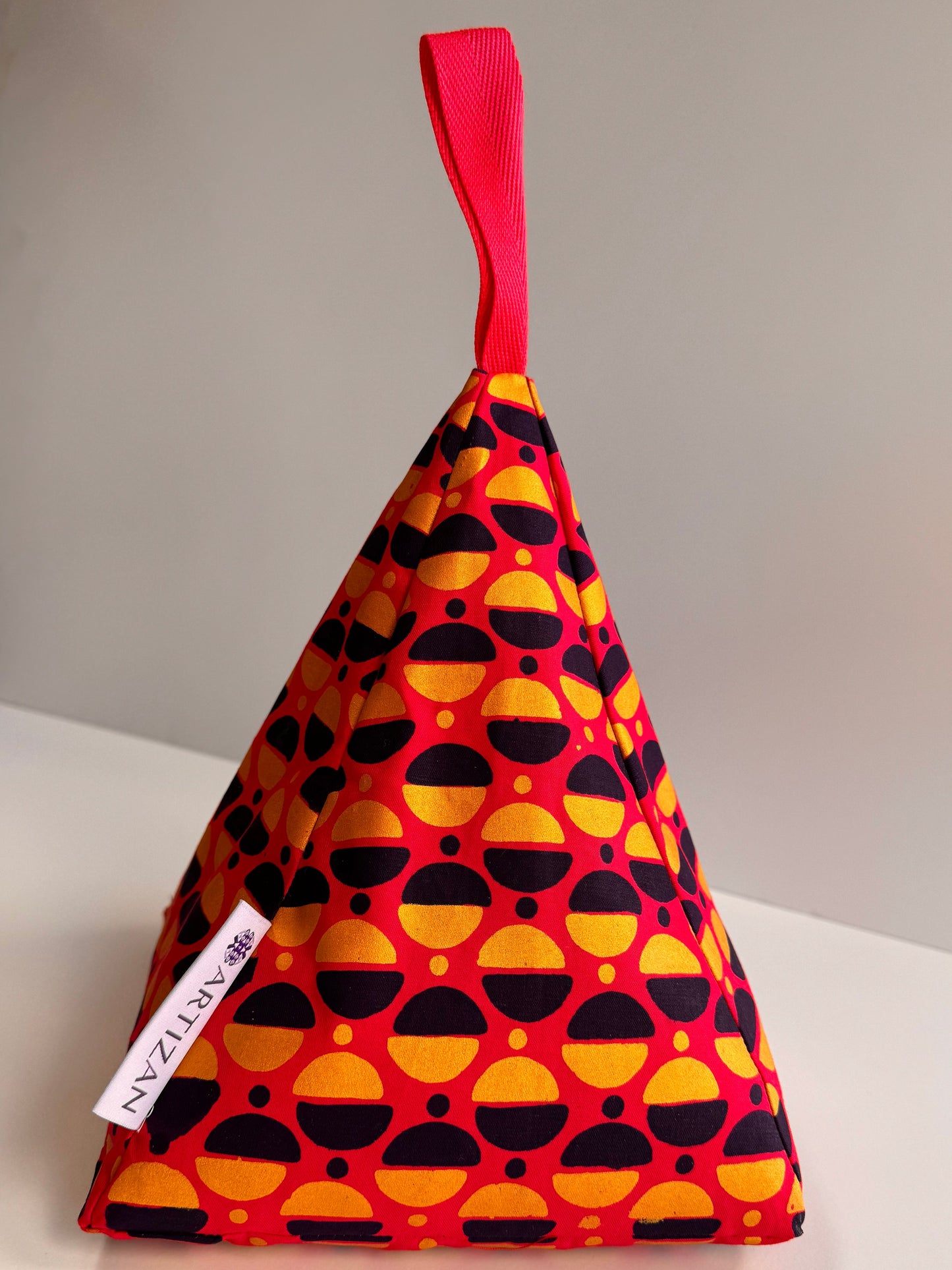 Pyramid-shaped doorstop in pink fabric with gold and navy blue semicircles printed on.