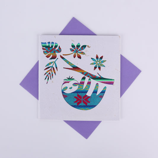 Colourful patterned cutout on a white card showing a sloth hanging from a tree with a purple envelope underneath