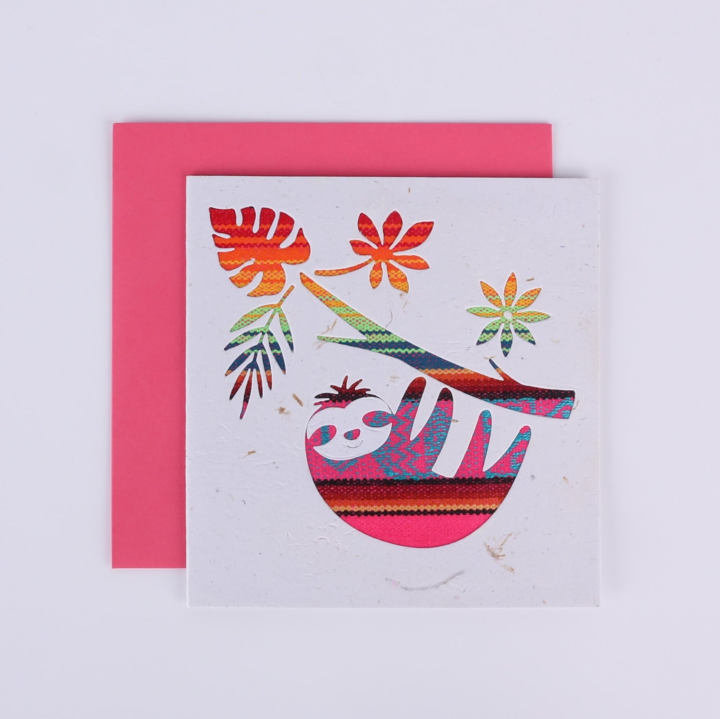 Colourful patterned cutout on a white card showing a sloth hanging from a tree with a pink envelope underneath