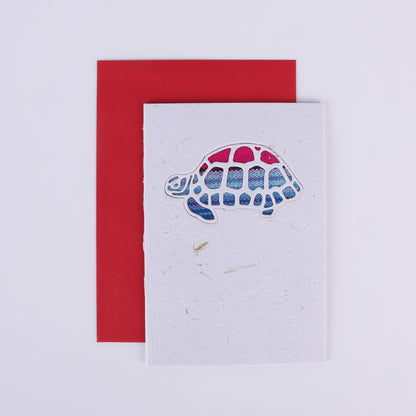 Colourful patterned tortoise cutout on a white card with a red envelope underneath