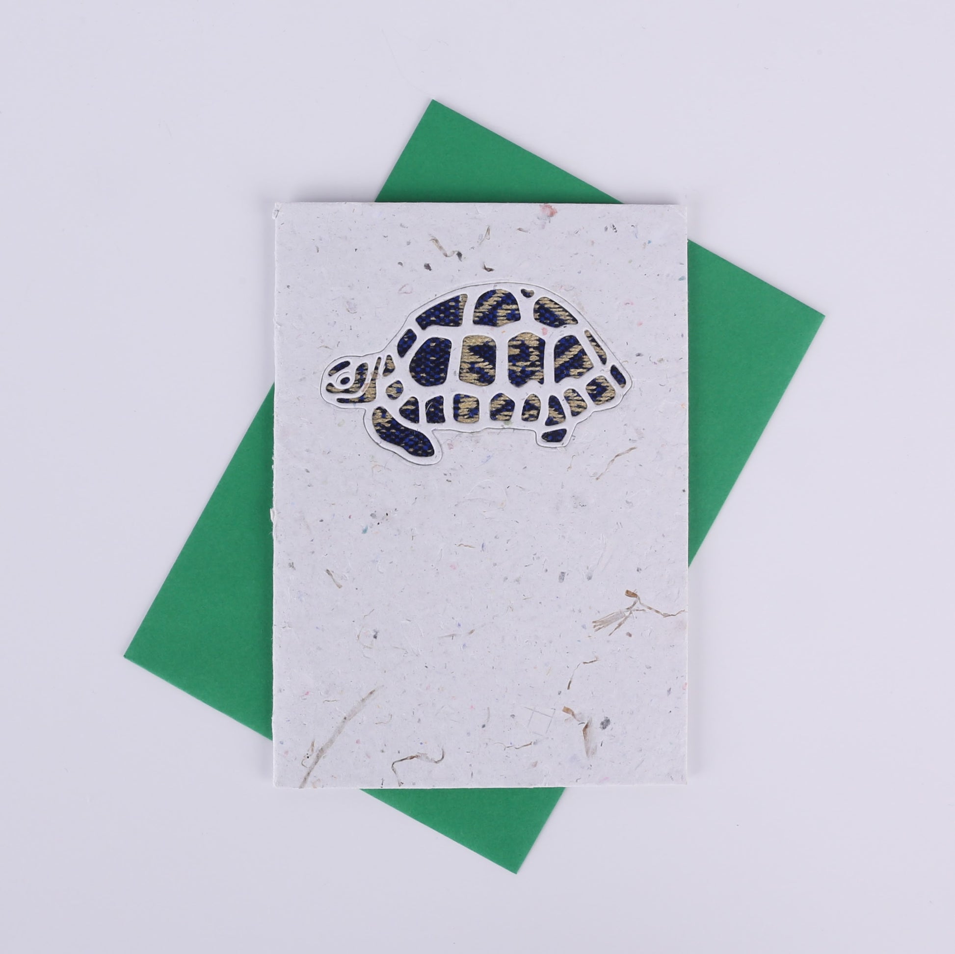 Colourful patterned tortoise cutout on a white card with a green envelope underneath