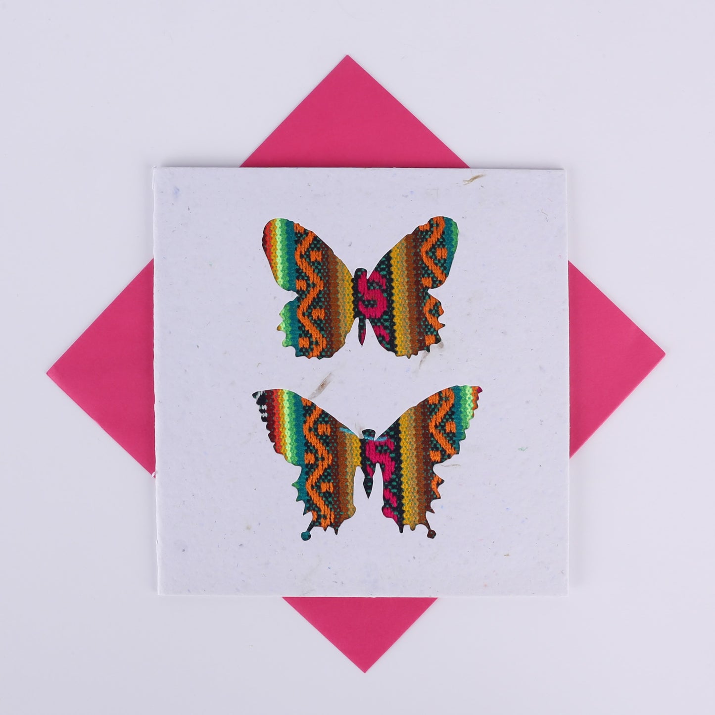 Colourful patterned butterfly cutouts on a white card with a pink envelope underneath