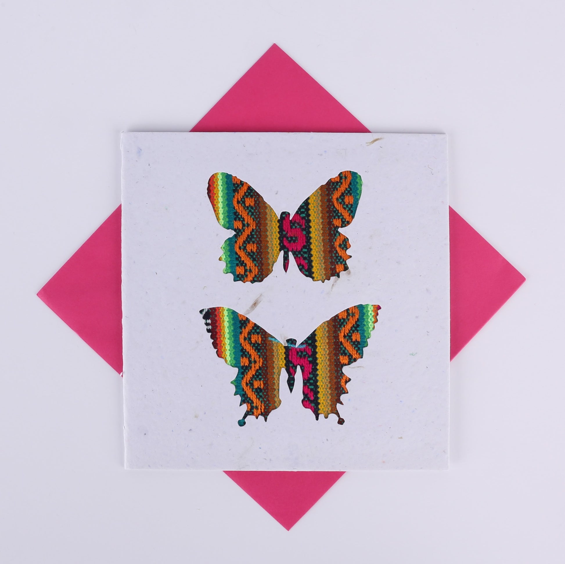 Colourful patterned butterfly cutouts on a white card with a pink envelope underneath